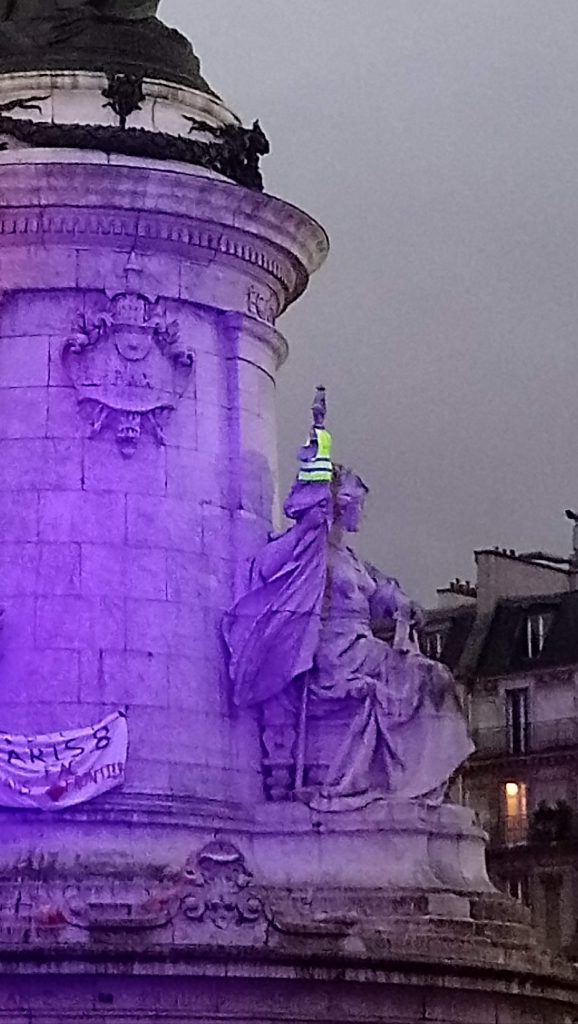 Vue partielle de la statue au centre de la Place de la République, Paris où l'on voit un gilet jaune porté sur le bras de la statue