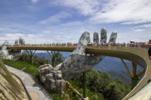 Une foule de touristes sur le pont de Da-Nang (Vietnam), une passerelle dorée se tenant deux mains géantes en pierrre, avec des vues des montagnes