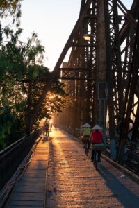 Au coucher du soleil, deux cyclistes s'éloignent sur un vieux pont à hautes poutrelles en bois et métal