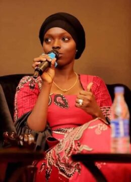 Hadja Idrissa Bah, jeune animatrice média et activiste guinéenne, en robe rouge et turban noir, avec un micro à la main