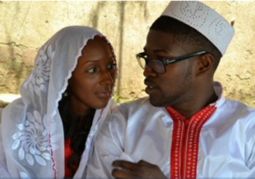 Un couple se regarde dans les yeux lors d'un mariage soussou en Guinée, la jeune femme porte une voile blanche brodée ouverte, le marié qui a des lunettes porte un chapeau cylindrique blanc et un jellaba blanc et rouge