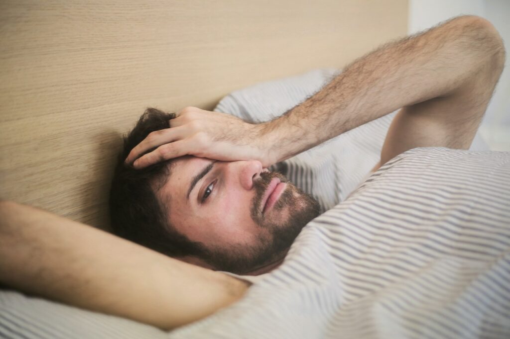 Un jeune homme qui vient de se réveiller le matin, il a le main au front et le regard indisposé comme s'il a passé une mauvaise nuit