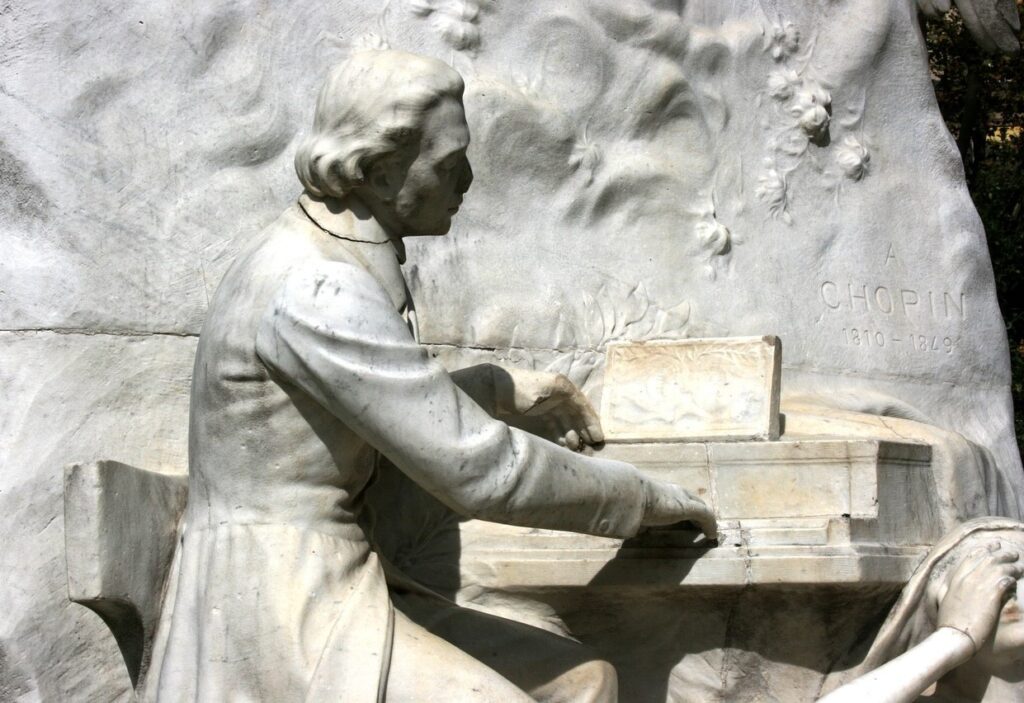 Détail du monument sculpté représentant le compositeur et pianiste Frédéric Chopin. La figure de Chopin assis et jouant du piano est vue de profil, la main gauche se lève, la main droite posé sur le clavier.