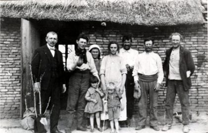 Une famille de 6 adultes et 2 enfants devant une petite maison à toit de chaume (photo en noir et blanc, fin du 19e siècle)