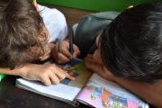 Deux enfants dont l'un tient un stylo se penchent sur un livre avec des images