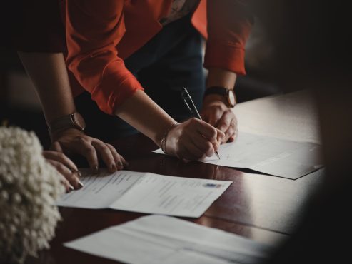 On voit les mains de 2 personnes appuyées sur une table, en train de remplir des feuilles d'un formulaire