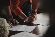 On voit les mains de 2 personnes appuyées sur une table, en train de remplir des feuilles d'un formulaire